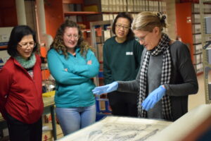 Three teachers watch archivist present a document. Photo is linked to open new webpage on Heritage in Schools Program.